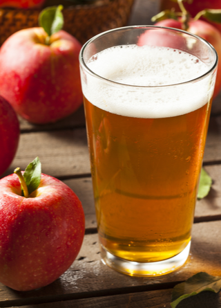 Tall glass of hard apple cider surrounded by apples, ready to drink. 
