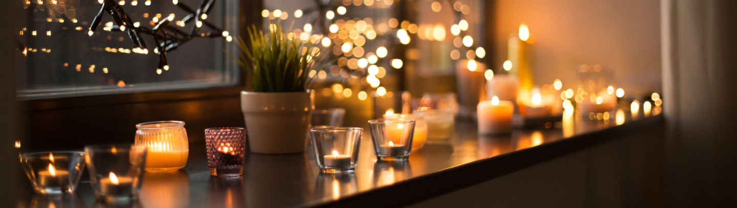 Tea light candles in holders with Christmas lights hanging in a window.