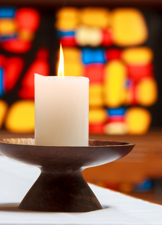 Burning white candle in front of a stained glass window