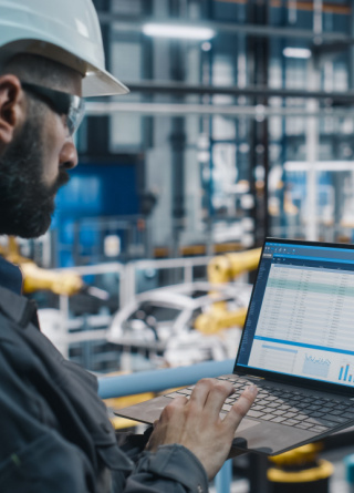 Worker looks at computer while standing in manufacturing plant. 