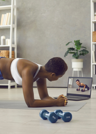 Young woman in workout clothes is watching a trainer on her laptop.