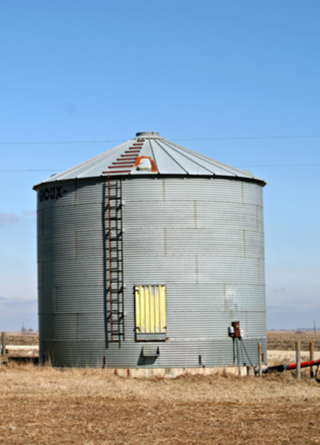 Two gray grain bins located on a midwestern farm.