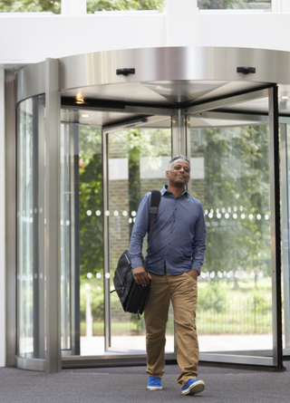 Man with messenger bag over right shoulder enters office building through revolving door, not worried about indoor air quality.