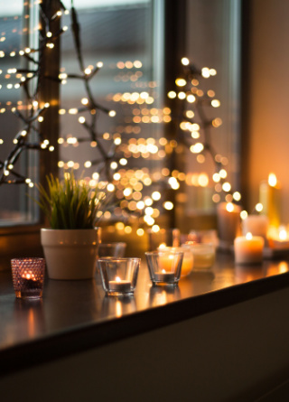 Tea light candles in holders with Christmas lights hanging in a window.