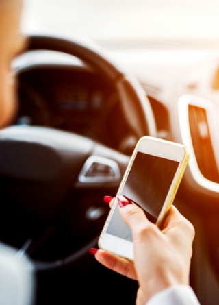 Businesswoman looks down at her phone while behind the wheel.