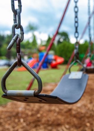 Closeup picture of a swing in a park for kids. Kids swinging in the blurry background. 