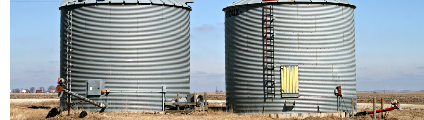 Two gray grain bins located on a midwestern farm.