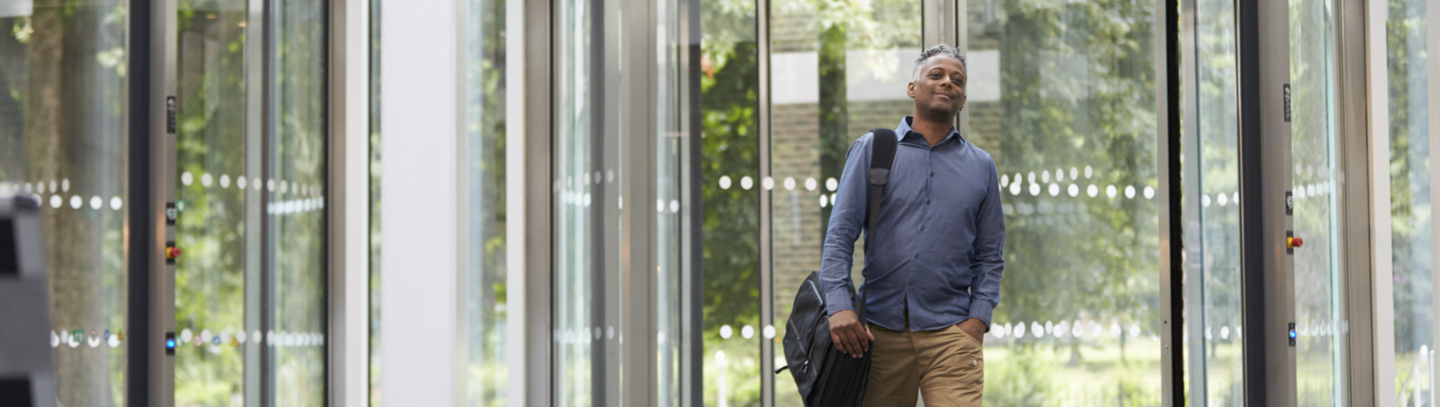 Man with messenger bag over right shoulder enters office building through revolving door, not worried about indoor air quality.