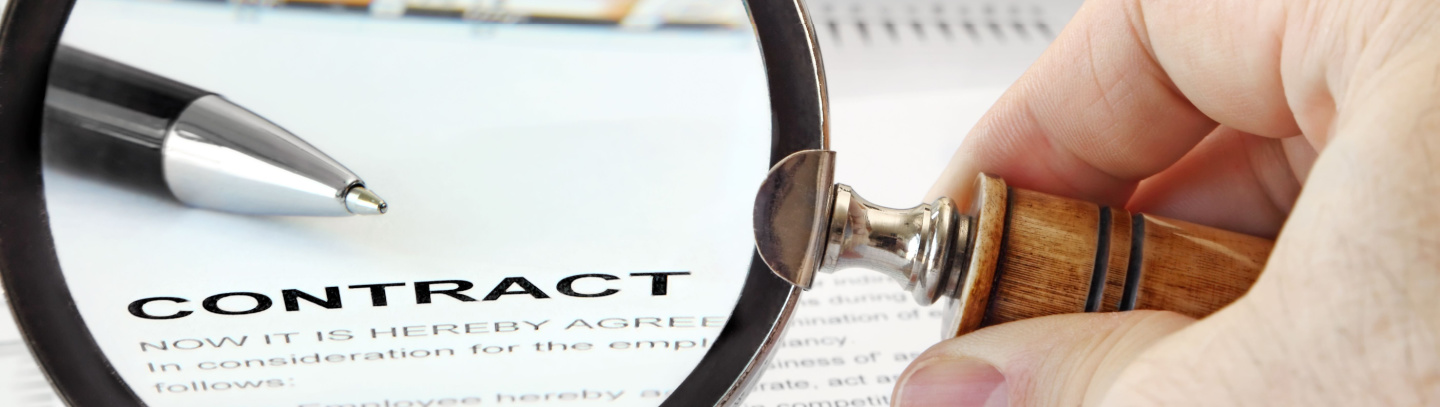 Magnifying glass over contract agreement with pen in view and more papers in the background.