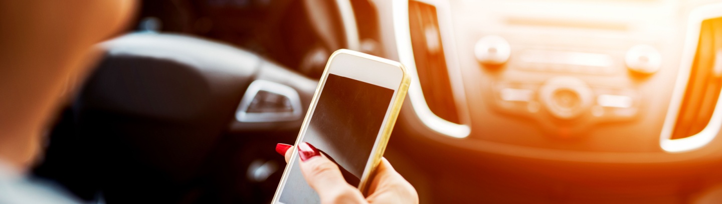 Businesswoman looks down at her phone while behind the wheel.