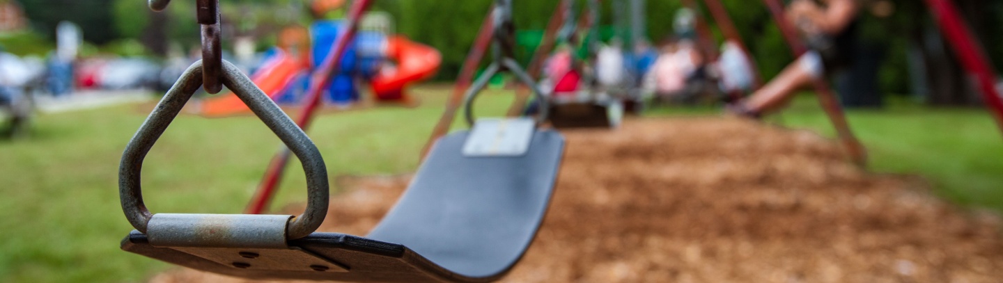 Closeup picture of a swing in a park for kids. Kids swinging in the blurry background. 