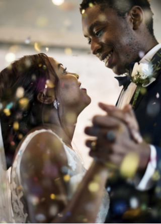 Young couple is dancing first dance at a nighttime wedding reception, surrounded by confetti and guests. 