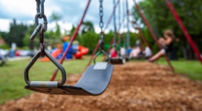 Closeup picture of a swing in a park for kids. Kids swinging in the blurry background. 