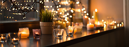 Tea light candles in holders with Christmas lights hanging in a window.