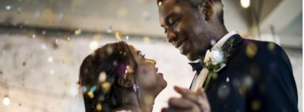 Young couple is dancing first dance at a nighttime wedding reception, surrounded by confetti and guests. 