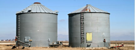 Two gray grain bins located on a midwestern farm.