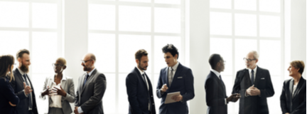 Nine professionally attired women and men stand in front of a large window wall discussing non-profit board insurance options.