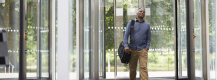 Man with messenger bag over right shoulder enters office building through revolving door, not worried about indoor air quality.