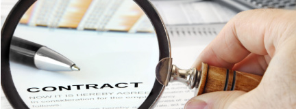 Magnifying glass over contract agreement with pen in view and more papers in the background.