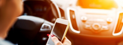 Businesswoman looks down at her phone while behind the wheel.