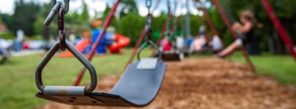 Closeup picture of a swing in a park for kids. Kids swinging in the blurry background. 