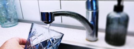 Person pouring drinking water from the tap into a glass 