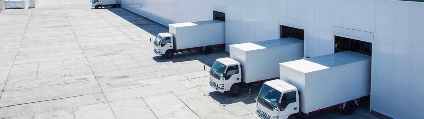 White box trucks lined up in garage doors of a warehouse.  