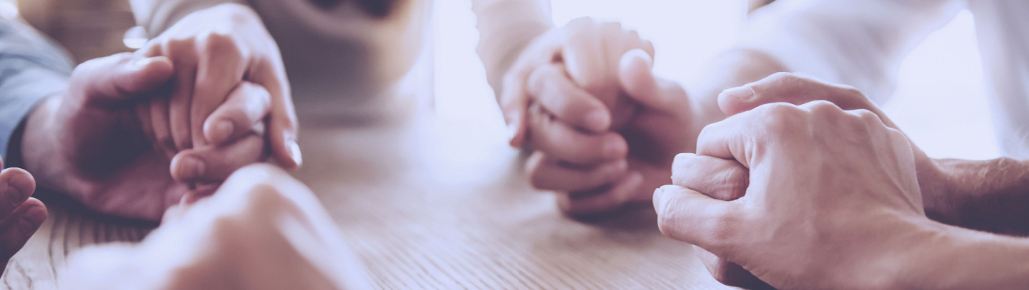 Circle of adults holding hands at a table. 