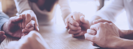 Circle of adults holding hands at a table. 