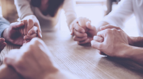 Circle of adults holding hands at a table. 