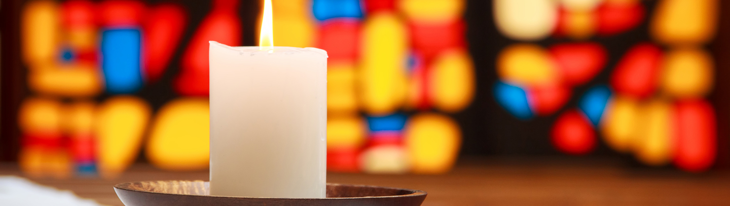 Burning white candle in front of a stained glass window