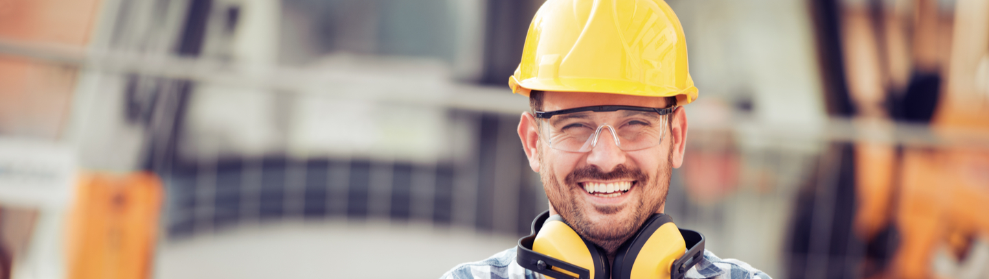 Smiling construction worker wearing hard hat in front of bulldozer. 