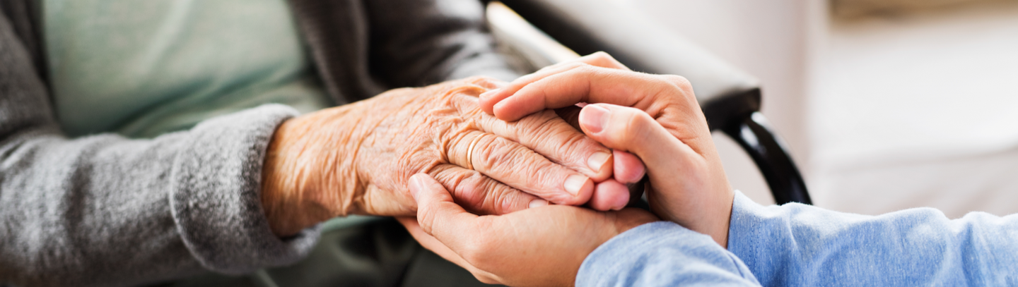 Close-up of an elderly woman in a wheelchair holding hands with a younger person.