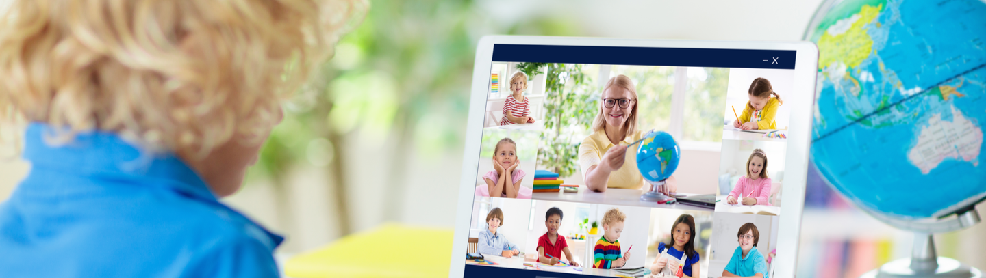 Little boy sitting at desk looking at the computer monitor which shows his online zoom class