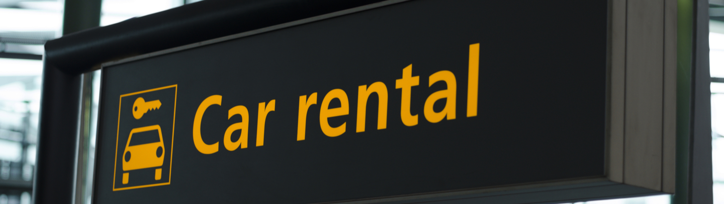 Yellow and black car rent sign with car icon and arrow pointing direction to go hanging from airport ceiling. 