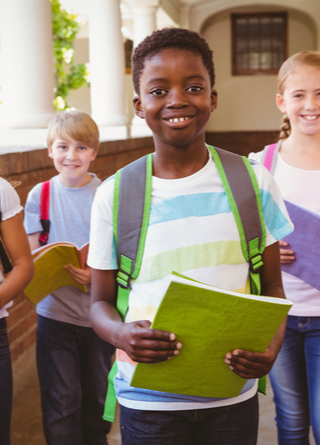 Group of four elementary age school children wearing backpacks in outdoor corridor, looking at camera.   