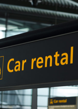 Yellow and black car rent sign with car icon and arrow pointing direction to go hanging from airport ceiling. 