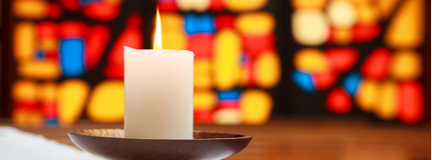 Burning white candle in front of a stained glass window