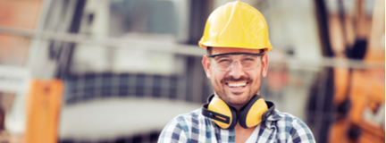 Smiling construction worker wearing hard hat in front of bulldozer. 