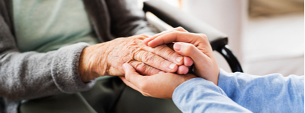 Close-up of an elderly woman in a wheelchair holding hands with a younger person.