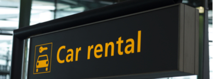 Yellow and black car rent sign with car icon and arrow pointing direction to go hanging from airport ceiling. 