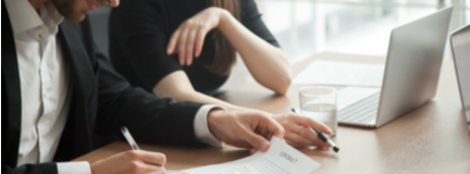 Businessman and woman look over the contract on the desk with a laptop.