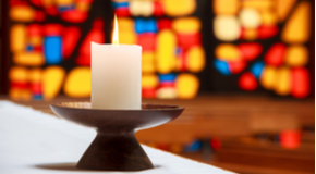 Burning white candle in front of a stained glass window